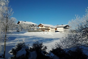 Eine verschneite Landschaft mit einem großen Gebäude, das viele Fenster und einen markanten Eingang hat.