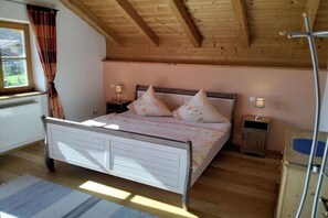 Ein Schlafzimmer mit Holzbalkendecke, einem Bett mit Kissen, Nachttischlampen und einem Fenster mit Vorhängen.