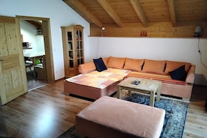 Ein gemütliches Zimmer mit Holzbalkendecke, einem großen orangefarbenen Sofa, einem kleinen Tisch und einem Schrank.