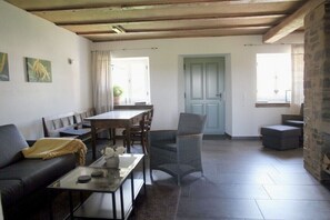 Ein Wohnzimmer mit einer Couch, einem Couchtisch, einem Esstisch mit Stühlen, einer Steinwand und einer Tür.