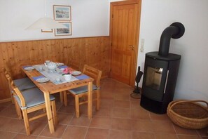 Ein Holzesstisch mit Stühlen, ein schwarzer Holzofen und eine Tür in einem Zimmer mit Holzvertäfelung.