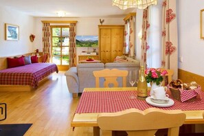 Ein gemütliches Zimmer mit Bett, Sofa, Esstisch und Bergblick durch das Fenster.