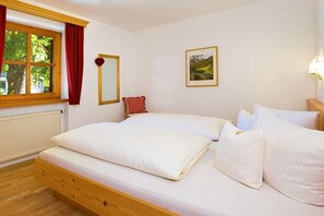 Ein Schlafzimmer mit einem hölzernen Bett, weißer Bettwäsche, einem Fenster mit roten Vorhängen, einem gerahmten Bild an der Wand und einer Heizung.