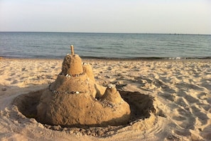Ein Sandburg am Strand, im Hintergrund das Meer.