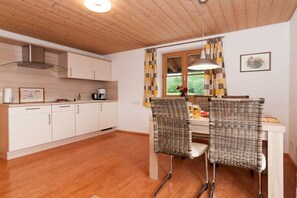 A kitchen with white cabinets, a stainless steel range hood, and a dining area with wicker chairs and a table. - Holiday apartment with 1 bedroom (Bad Wiessee)