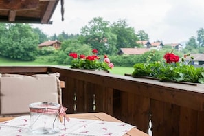 A wooden deck with a table, a glass jar with a ribbon, and flower planters with red flowers. - Holiday apartment with 1 bedroom (Bad Wiessee)