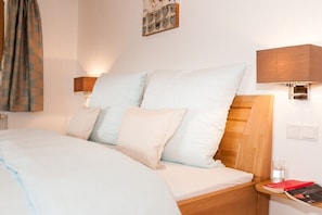 A neatly made bed with a wooden headboard, two bedside lamps, a small bedside table with a book and glass, and a wall-mounted picture frame. - Holiday apartment with 1 bedroom (Bad Wiessee)