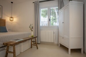 Ein Schlafzimmer mit Bett, Nachttisch, Lampe, Fenster, Heizkörper und Kleiderschrank.