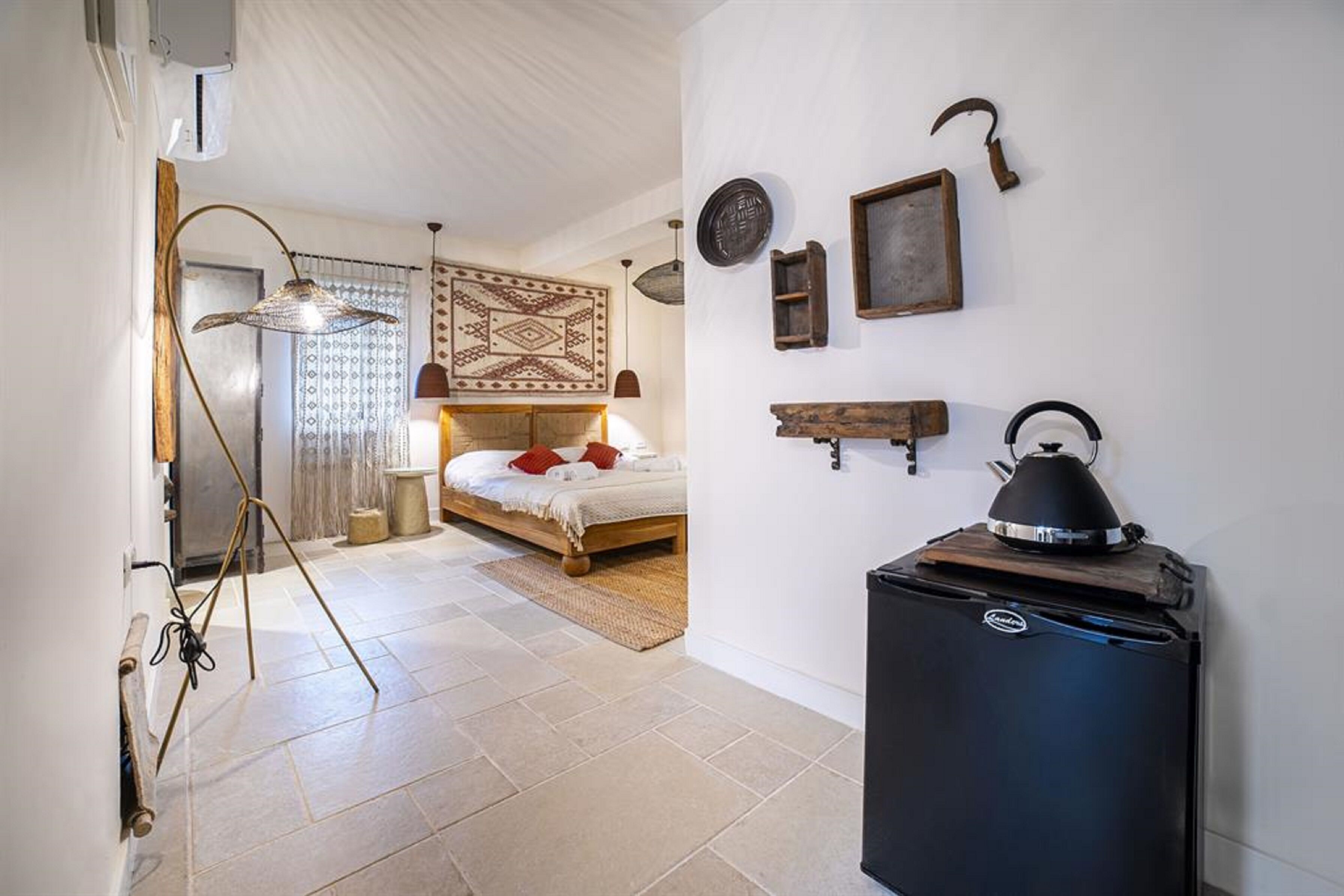 A bedroom with a bed, a small refrigerator, a lamp, and a wall-mounted shelf.