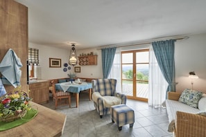 A cozy room with a dining table, chairs, a sofa, and a view through a large window. - Holiday apartment with 1 bedroom (Wegscheid)
