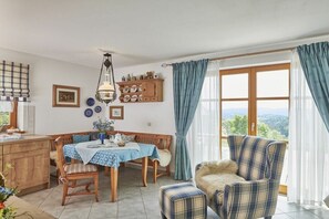 A dining area with a table, chairs, a bench, a sofa, and a view through a large window. - Holiday apartment with 1 bedroom (Wegscheid)