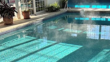 Une piscine intérieure à l’eau d’un bleu cristallin, dont le sol est décoré d’un motif de cadran solaire, et des plantes en pot qui ornent l’espace autour de la piscine.