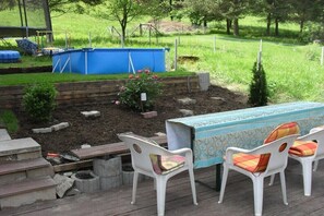 Eine Terrasse mit Tisch und Stühlen, ein erhöhter Blumenkasten mit Pflanzen und ein blauer Behälter im Hintergrund.