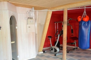 Ein Fitnessraum mit Trainingsgeräten, einem Boxsack und einer Tür zu einem weiteren Raum.