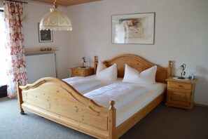 Ein hölzernes Himmelbett mit weißen Leinen, zwei Nachttische mit Lampen, eine Heizung und ein gerahmtes Bild an der Wand.