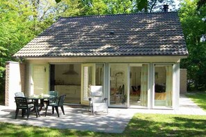 Ein Haus mit Ziegeldach, einer überdachten Terrasse mit Tisch und Stühlen sowie einer Glastür, die zu einem Innenraum führt.