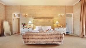 Un grand lit recouvert d’une couverture moelleuse, deux tables de chevet avec des lampes, un miroir et une tête de lit décorative.
