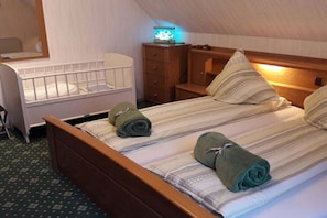 Ein Schlafzimmer mit einem Reisebett, einem Bett mit gerollten Handtüchern, einem Nachttisch, einer Kommode und einer Lampe.