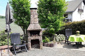 Eine Außenpatio mit einem Kamin aus Stein, zwei Stühlen, einem Tisch mit grüner Tischdecke und einem Topfpflanzen.