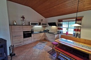 A kitchen with wooden cabinets, a stove, a sink, and a window with curtains. - Holiday home with 2 bedrooms (Neuschönau)