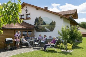 Ein Gebäude mit Wandgemälde einer Landschaft, Sitzgelegenheiten im Freien und einer Grillanlage.
