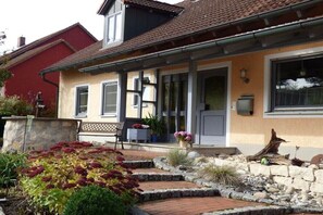 Ein Haus mit Veranda, einer Bank, Topfpflanzen und einem Kiesweg.