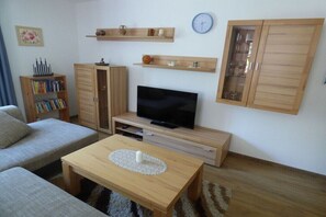 Ein Wohnzimmer mit einer Couch, einem Couchtisch, einem Fernseher, Holzregalen und einem Schrank.