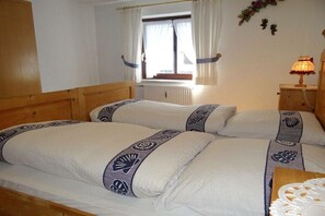 Ein Zimmer mit zwei Betten, einem fensterbelaubten Fenster, einem Heizkörper und einem Nachttisch mit Lampe.
