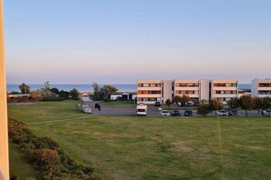 A residential building with multiple floors, a parking area, and a grassy field in the foreground. - Apartment with 1 bedroom (Fehmarn\/ Burgtiefe)