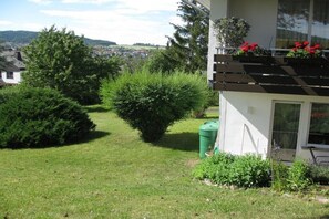Un immobile residenziale con un prato curato, un grande albero e un balcone con fiori rossi.