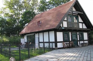 A traditional half-timbered house with a sloped roof, a satellite dish, and a paved courtyard with outdoor furniture. - Timber-framed cottage on the Salzhaff (Boiensdorf\/OT Stove)