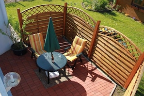 A patio with a wooden lattice fence, a round table, two chairs, and a green umbrella. - Holiday apartment - Bachmann (Hagenburg)