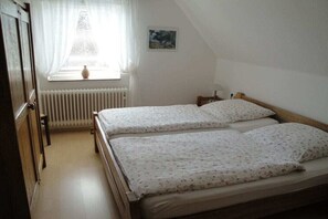 Ein Schlafzimmer mit zwei Betten, einem Heizkörper, einem Fenster mit Vorhängen und einem kleinen Gemälde an der Wand.
