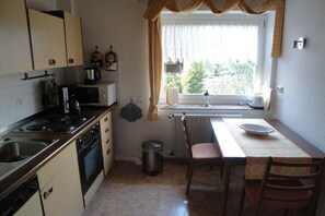 Eine kleine Küche mit Herd, Backofen, Mikrowelle und einem Fenster mit Vorhängen.