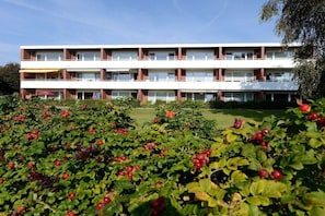 Ein mehrstöckiges Gebäude mit Balkonen, umgeben von einem Garten mit roten Beeren.