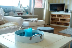 Ein Wohnzimmer mit einer Couch, einem Fernseher, einer Kaffeemaschine und einem kleinen Modell eines Segelboots.
