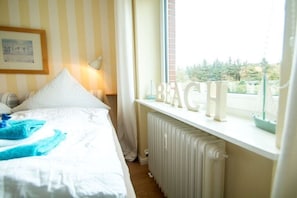 Ein Schlafzimmer mit Bett, Heizkörper, einem Fenster mit Vorhängen und einem an der Wand befestigten Schild.