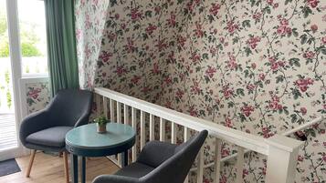A room with a wooden floor, two grey armchairs, a small round table, a white railing, and floral wallpaper.