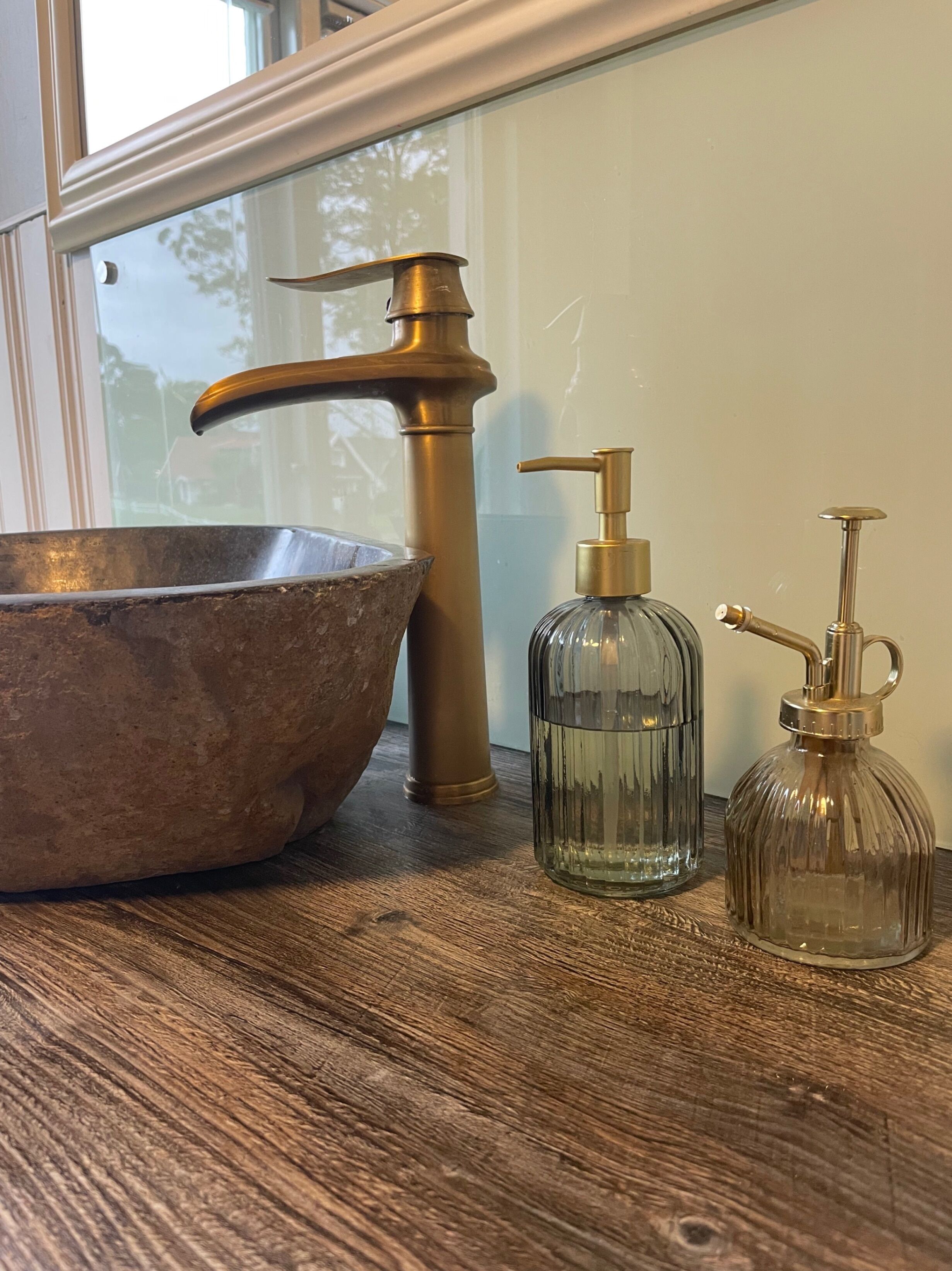 Un meuble-lavabo de salle de bain doté d’un grand lavabo en cuivre, d’un robinet en laiton et de deux distributeurs en verre.