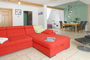 Un sofá seccional rojo, una mesa de comedor con sillas y una mesa redonda pequeña con una silla.