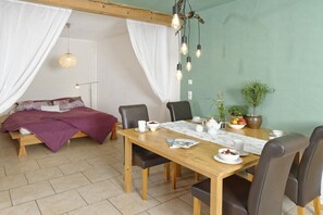 Ein Zimmer mit einem Bett, einem Esstisch mit Stühlen, einer Pendelleuchte und einer Zimmerpflanze.