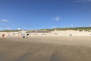 Ein Sandstrand mit Zelten und einem Gebäude im Hintergrund.