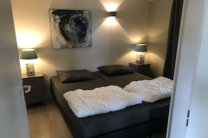 Ein Schlafzimmer mit zwei Betten, einem Bild an der Wand und zwei Nachttischlampen.