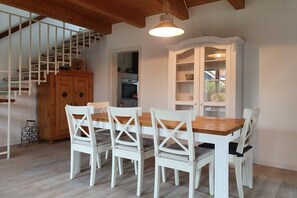 Ein Essbereich mit Holztisch und weißen Stühlen, eine Treppe mit Holzläufer und ein weißes Schrank mit Glastüren.