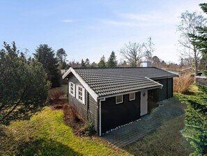 Ein eingeschossiges Haus mit dunkler Fassade, einem Ziegeldach und einer kleinen Veranda.