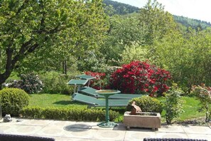 Ein Garten mit Vogeltränke, Statue und einem rot blühenden Strauch.