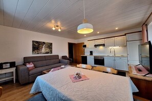 Ein modernes Zimmer mit einem Bett, einer Couch, einem Esstisch und einer Küchenzeile.