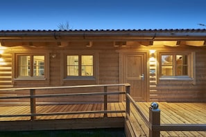 A wooden cabin with a deck, large windows, and a door.