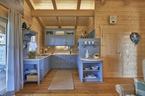 A wooden cabin interior with a kitchen featuring blue cabinets, a wooden ceiling, and a door with a wreath.