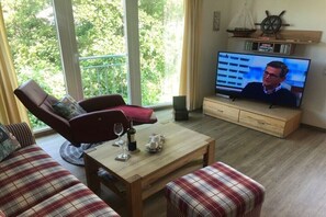 Ein Wohnzimmer mit Sofa, Sessel, Couchtisch und Fernseher.